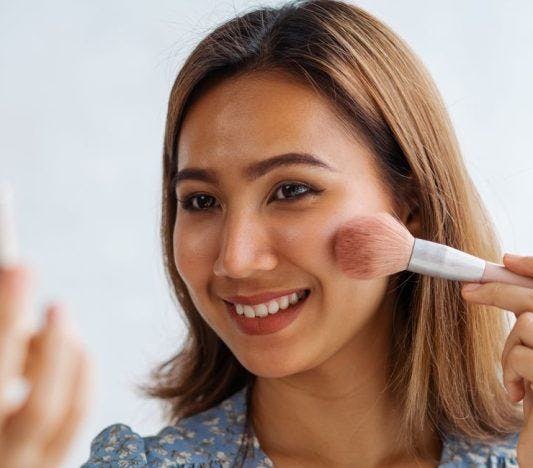 Smiling woman applying blush with a brush.