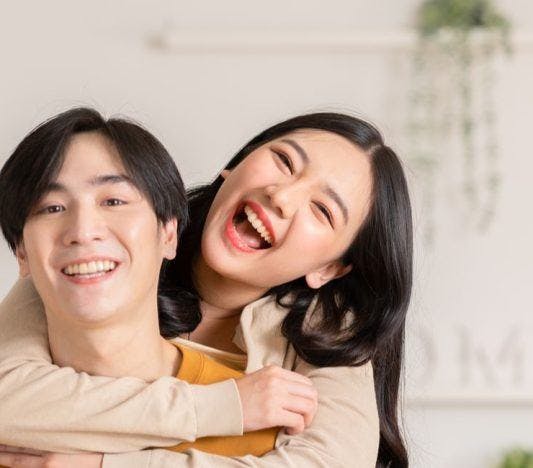 Asian couple smiling while man is carrying woman on his back.