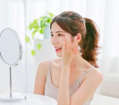 Woman smiling and touching the side of her face in front of a mirror.