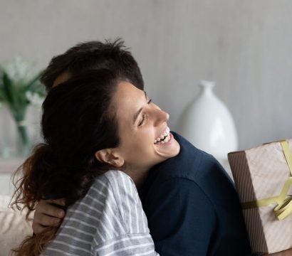 Smiling woman holding a gift box and hugging with partner.