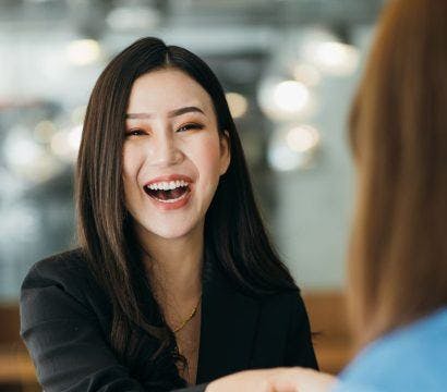 Woman smiling as she shakes hands with someone.