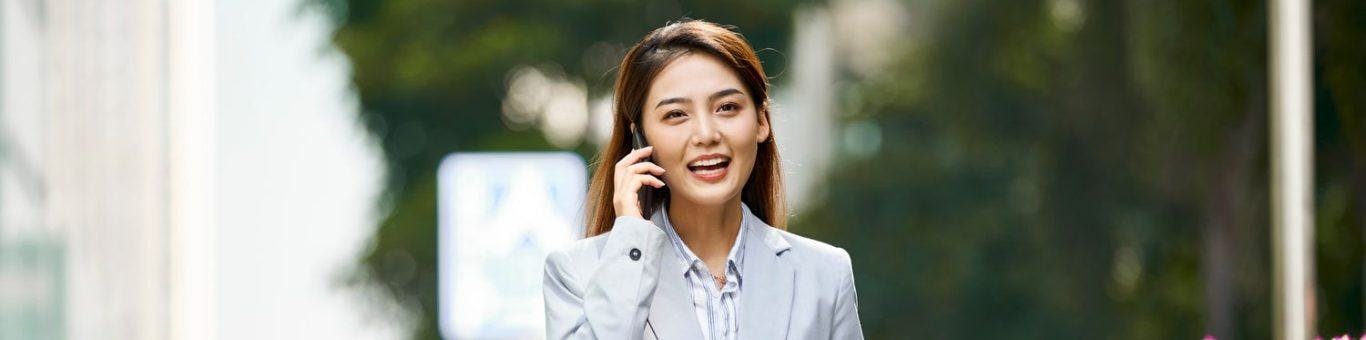 Smiling businesswoman in grey on the phone while walking outdoors.
