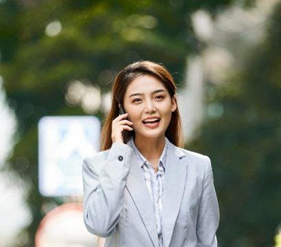 Smiling businesswoman in grey on the phone while walking outdoors.