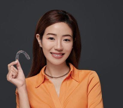 A woman holding clear aligners and smiling.