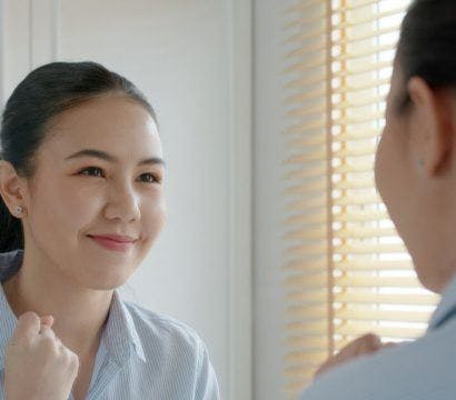 Woman smiling at herself in the mirror with her first up.
