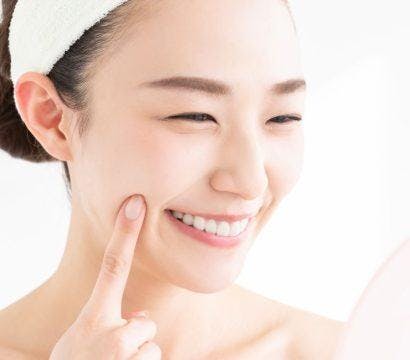 Smiling woman touching her face with her index finger in the bathroom.