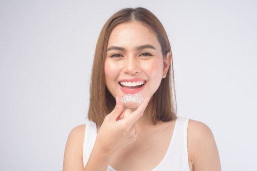 Smiling young woman holding up dental aligners against a white background.