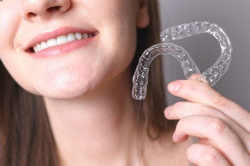 A woman smiling and holding up a pair of clear aligners.