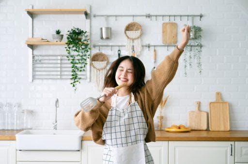 Woman happily holding a ladle in one hand and raising the other.