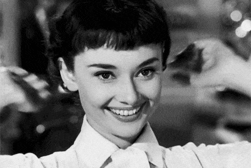 Audrey Hepburn smiling and resting her hands on her head.