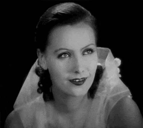 Black-and-white gif of Greta Garbo smiling shyly.