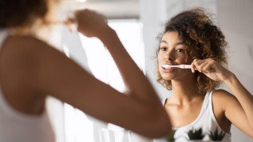 Woman with curly hair smiling and brushing her teeth in front of mirror.