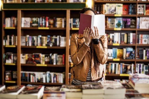 Woman holding up book in front of her face at a bookstore.