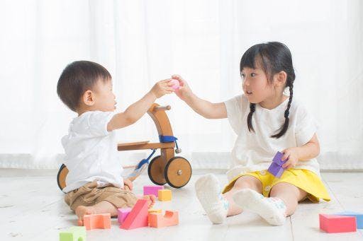 Two toddlers playing with blocks on the floor. 