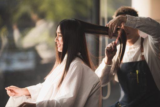 Male stylist cutting the hair of a smiling Asian woman. 