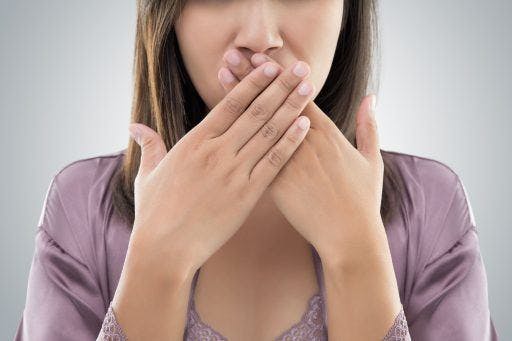 Closeup of a woman covering her mouth against a grey background.