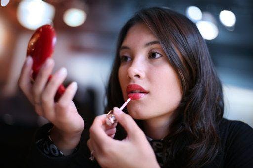A woman holding a compact mirror while applying red lipstick. 