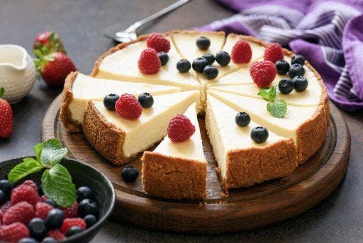 Cheesecake cut into slices with berries on top on a wooden board. 