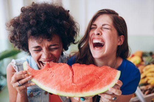 Two friends laughing while sharing watermelon.