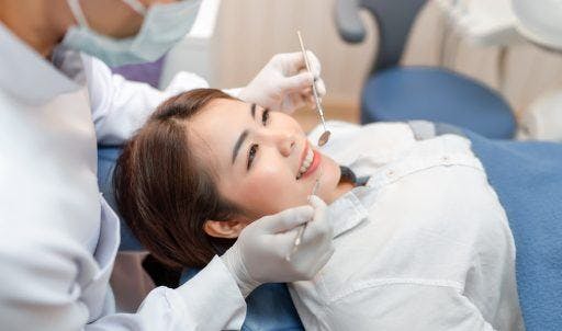 Asian woman getting her teeth checked and cleaned by a dentist.
