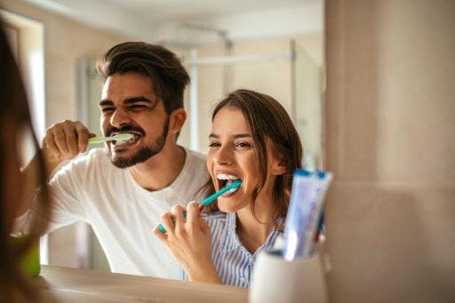 Man and woman brushing their teeth in front of a mirror.