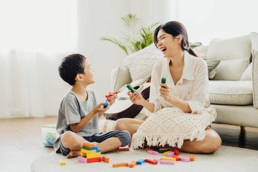 Asian mom and son playing blocks together on the floor in a bright room. 