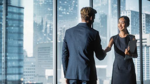 Male and female business associates happily shaking hands in an office.