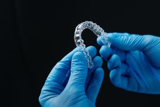 Two hands in blue surgical gloves holding clear aligners.