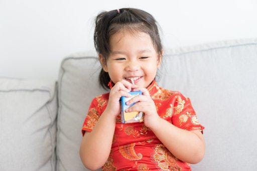 A girl drinking milk from a box with straw.