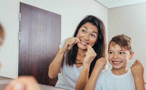 A woman and a child flossing together in front of a mirror.