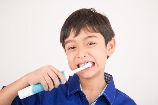 Little boy using an electric toothbrush against a white background.