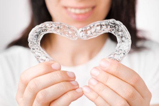 Closeup of a woman holding up dental aligners in the shape of a heart. 