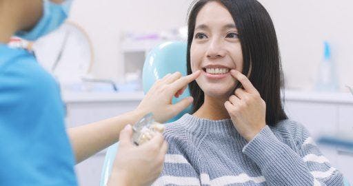 Woman at the dentist smiling and pointing to her teeth.