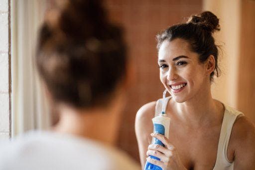 Young woman using a waterpik and smiling in front of a mirror.