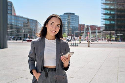 Asian woman in cropped top and suit smiling while holding phone. 
