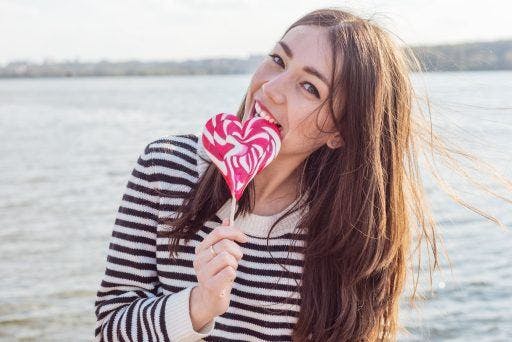 Woman biting into a heart-shaped lollipop.
