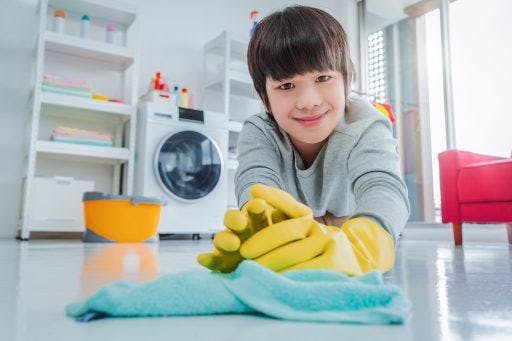 Young Asian boy with rubber gloves wipes the floor clean in his house.