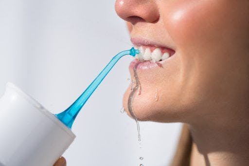 A closeup image of a woman’s teeth being cleaned by a portable water floss.