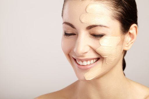 Smiling woman with smears of makeup on one side of her face against a white background.