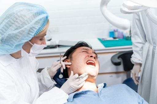 Photo of a dentist about to examine a young man patient on a dental chair at her clinic 