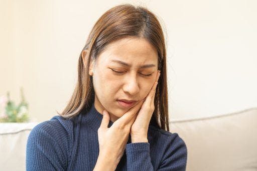 A woman in pain holding her cheek, ear, and jaw. 