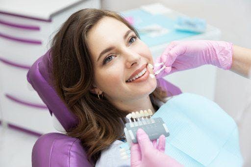Brunette woman in dentist’s clinic, as dentist holds up different-coloured enamel. 