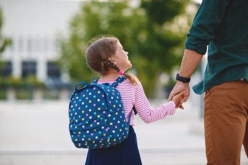 Little girl carrying polka-dotted backpack and holding her father's hand. 