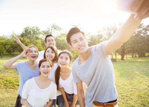 Group of friends, confidently smiling into the camera, taking a group selfie at the park