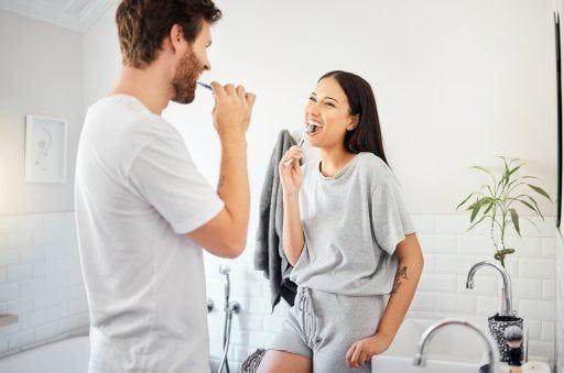 Photo of couple in bathroom, brushing their teeth happily