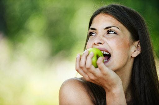 Portrait of a woman happily taking a bite out of a green apple. 