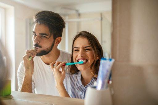 Young brunette couple brushing their teeth in front of mirror.