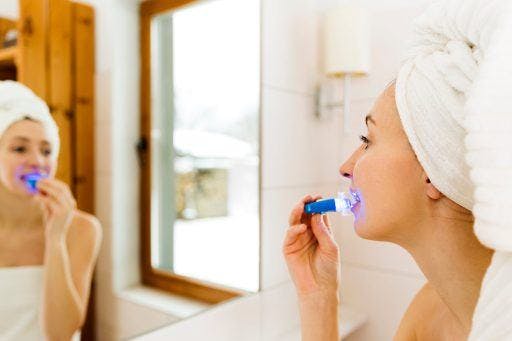 Woman using teeth whitening LED kit at home. 