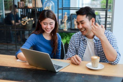 A smiling young couple checks out the woman's laptop while having coffee at a café. 