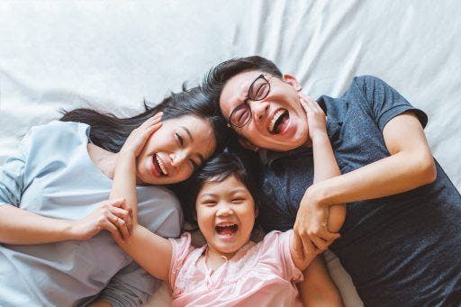 A young Asian family of three smiling for the camera while lying on a bed.